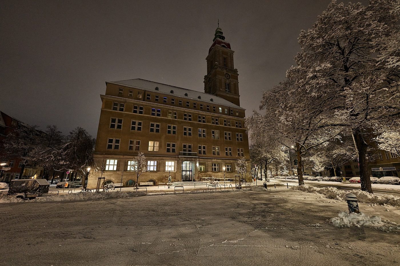 A historic town hall in Berlin at night with lit windows and entrance, snow on the square