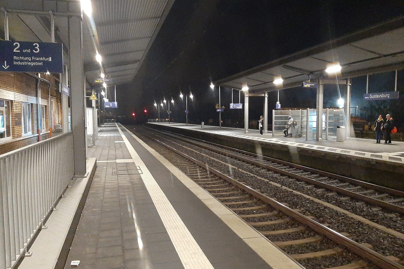 An empty railway platform at night under a long canopy with lamps