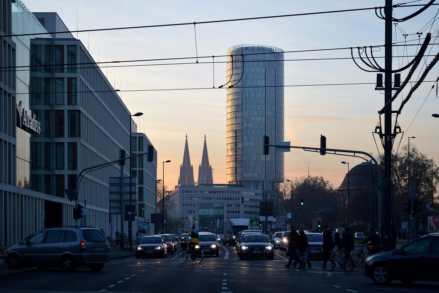 Eine Straße in Köln in der Abenddämmerung, Ampeln und Scheinwerfer, in der Ferne die Domtürme